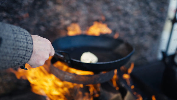 Melting butter in a cast iron pan over an open fire in winter, Luleå