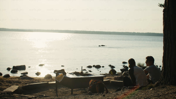 Romantic camping couple enjoying a scenic sunset by the lake in Luleå