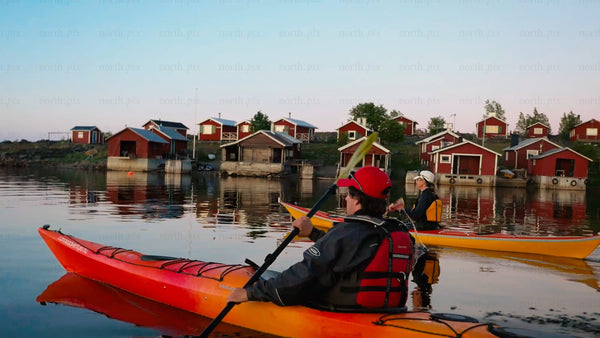 Kayaking past red cabins in the Luleå archipelago at twilight