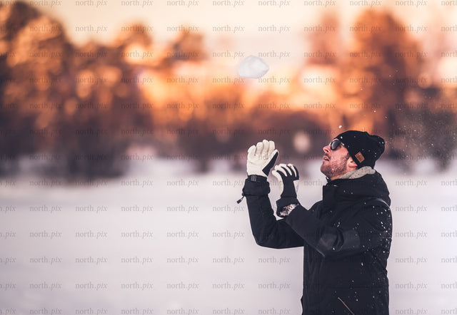 Man tossing snow in winter field at sunset