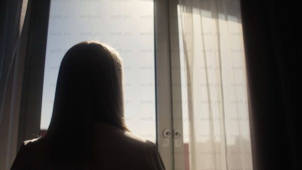 Woman looking out hotel window in morning sun