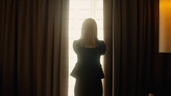 Businesswoman opens curtains in hotel room to bright sunny day