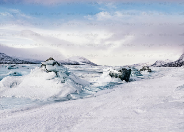 Snow-covered ice formations on a frozen lake with mountains