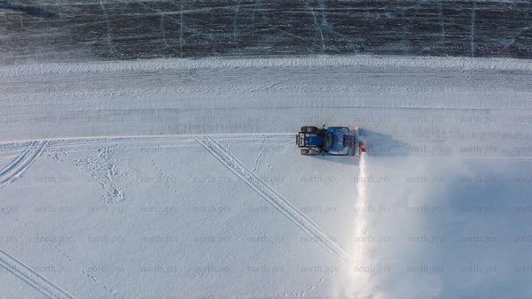 Aerial drone footage of snow blower clearing path on frozen lake in Luleå during winter