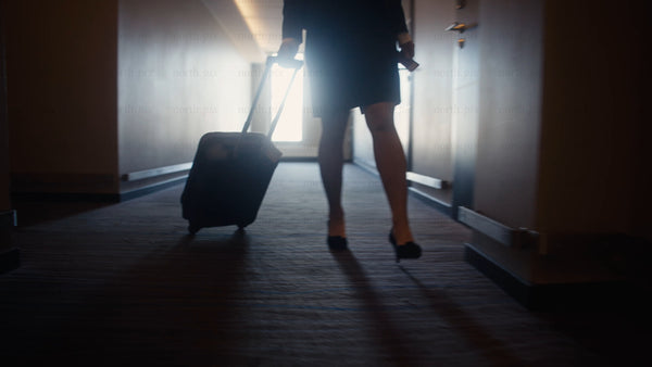 Businesswoman walking down hotel hallway with suitcase