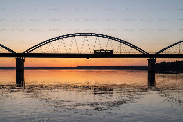 Tram crossing arch bridge over river at sunset