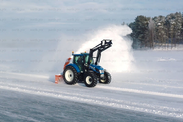 Blue tractor with snow plow clearing snow in open field under winter sky near forest
