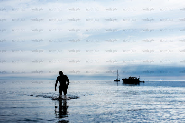 Man walking in shallow sea with anchored boats