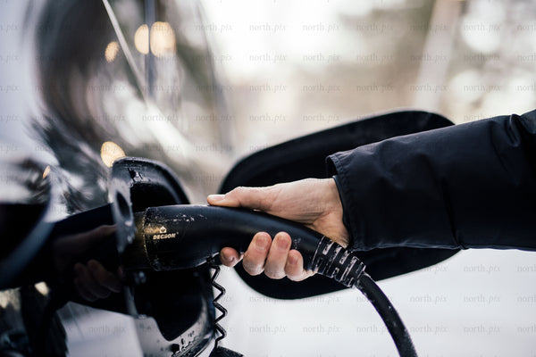 Person plugging electric car charger into vehicle in winter