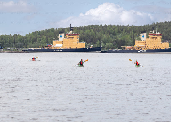 Kayakers paddling near docked icebreakers on overcast day