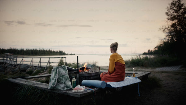 Summer evening in the Luleå archipelago: Woman relaxes by campfire at twilight