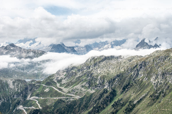 Winding mountain road through alpine ridges and clouds