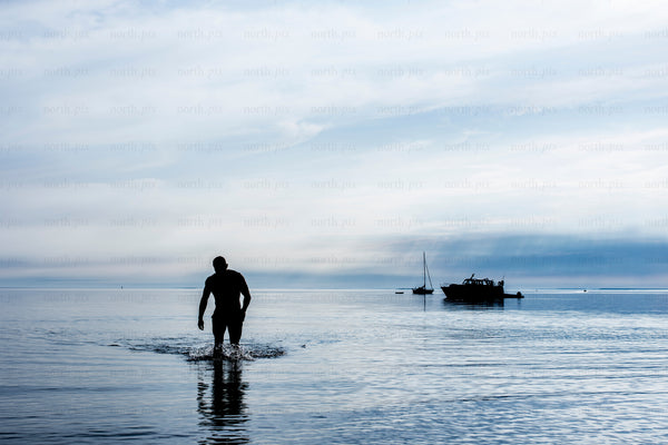 Man walking in shallow sea with anchored boats