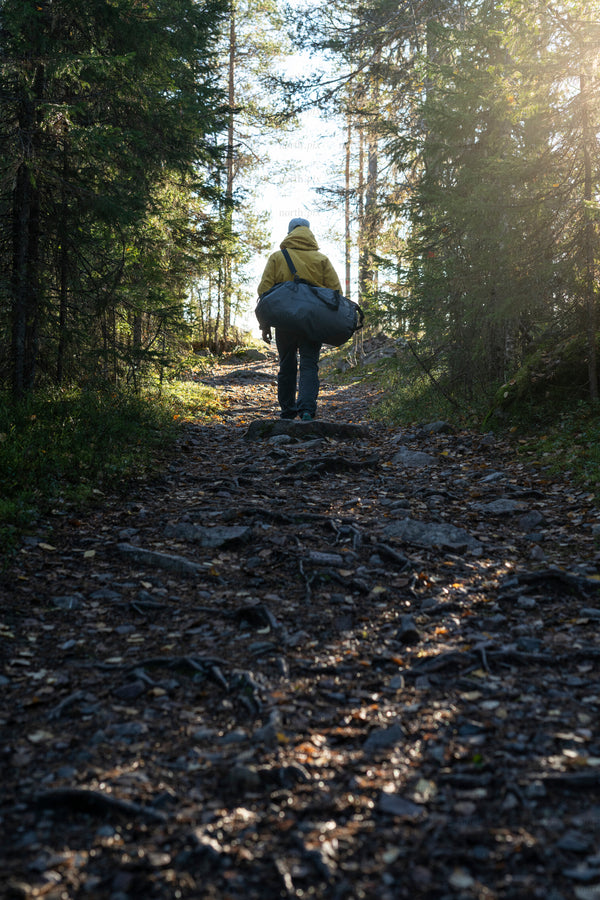 Person carrying duffel bag on forest trail in morning