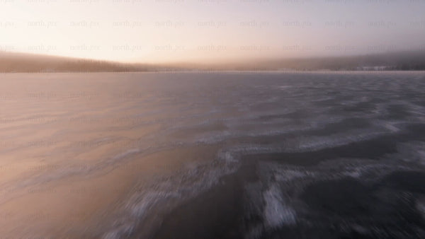 Low-level aerial drone footage over frozen lake at sunset in arvidsjaur