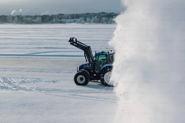 Blue tractor clearing snow in open field with large snow cloud in winter landscape