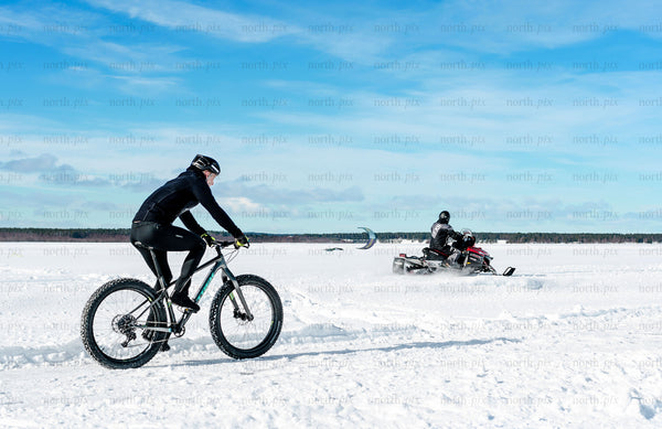Cyclist and snowmobile on a frozen lake in winter
