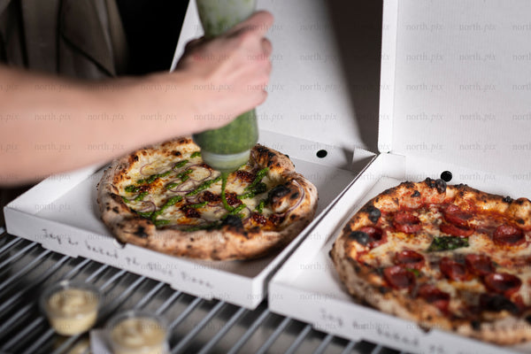 Hand squeezing pesto over pizza in takeout box