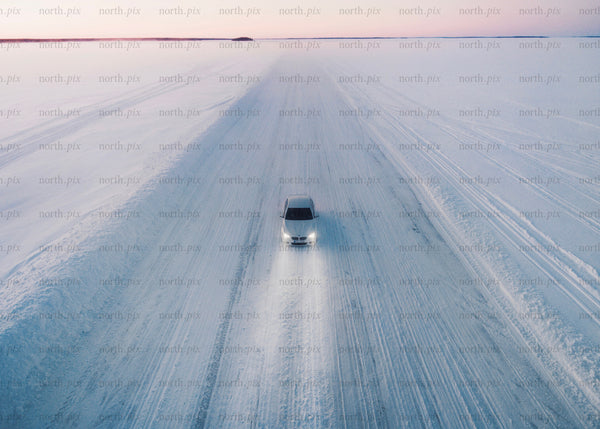 White car driving on a snowy ice road during sunset in winter