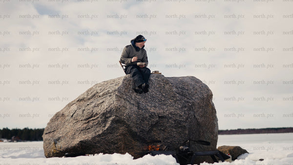 Man enjoys a warm drink by a fire on a frozen lake in the Luleå archipelago