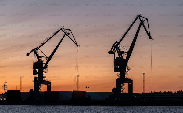 Two harbor cranes silhouetted against sunset sky at port of Luleå