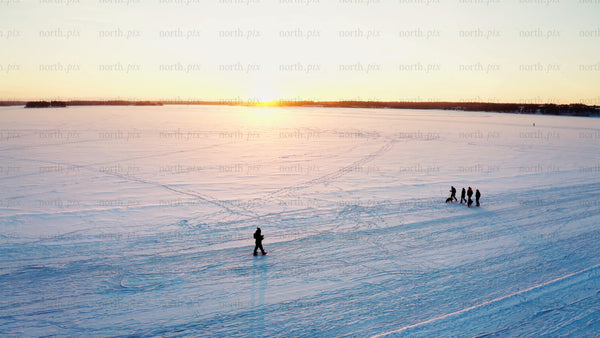 Friends enjoy a winter sunset walk on a frozen lake in Luleå