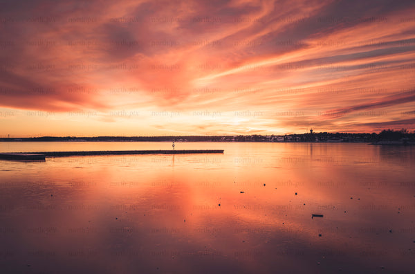 Sunset over frozen harbor with dock and town skyline