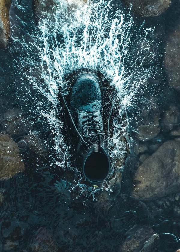 Black boot splashing water in shallow rocky stream