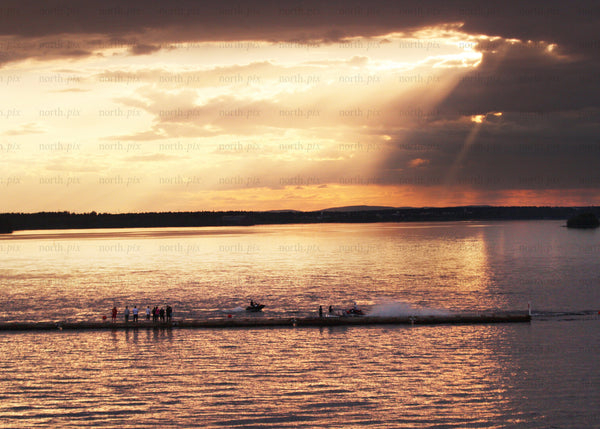 Golden sunset over water with people and jet ski present