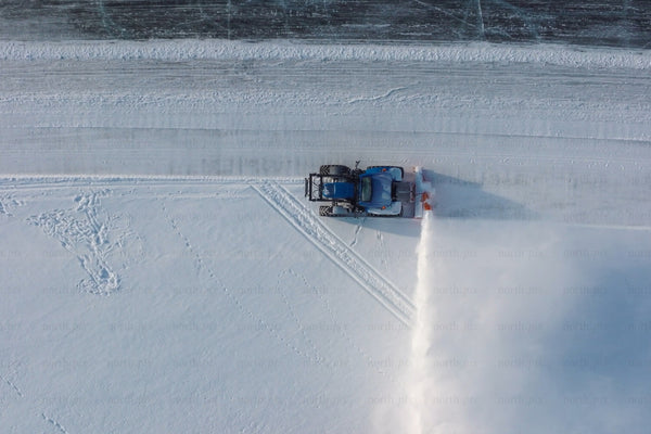 Snowplow clears snow on frozen water near Luleå city center — aerial winter cleanup