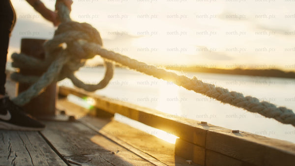 Securing mooring rope on wooden dock at sunset in Luleå