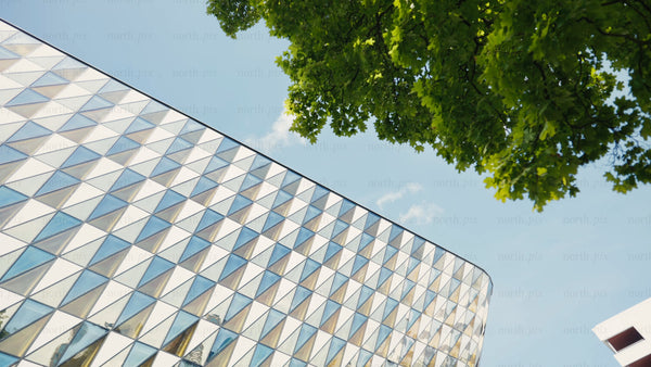 Modern glass building with triangular facade, green trees, and blue sky