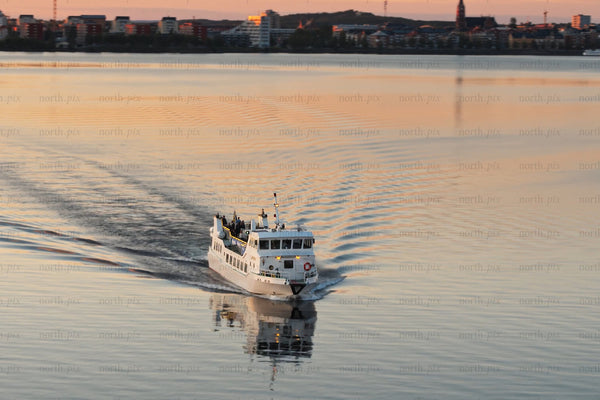 White ferry boat gliding across calm sunset waters near Luleå city center during evening light