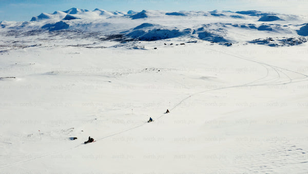 Snowmobiles riding across snowy landscape with mountains