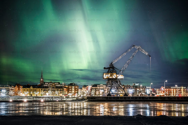 Northern Lights over harbor crane and city skyline at night