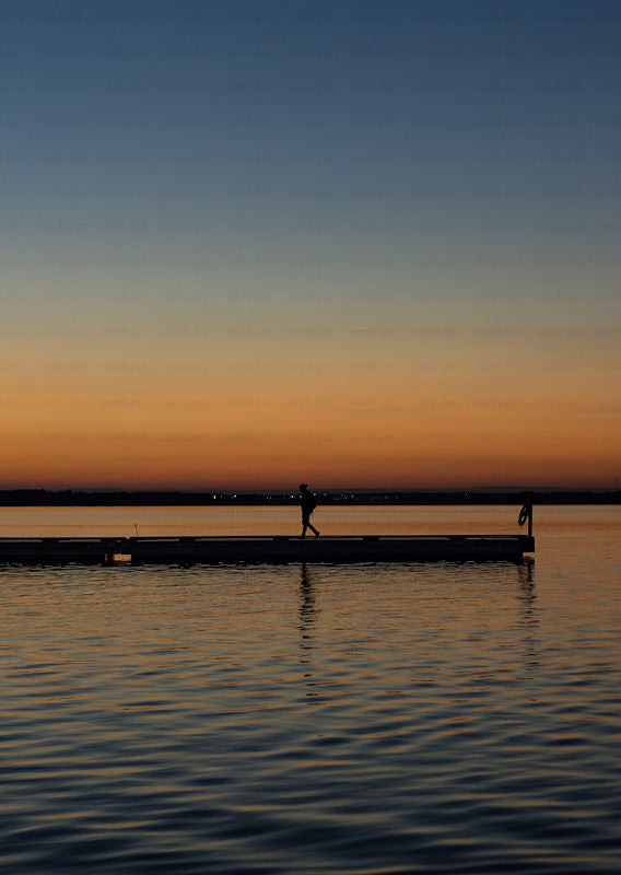 Person walking on pier at sunset