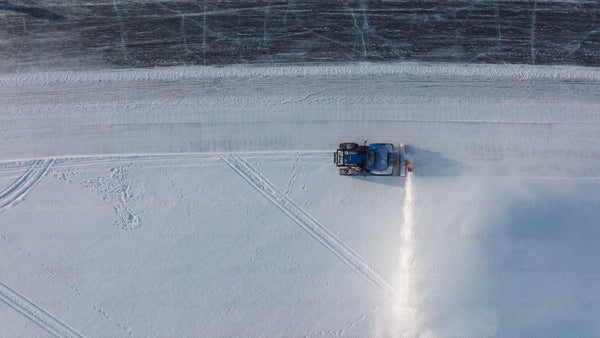 Aerial drone footage of snow blower clearing path on frozen lake in Luleå during winter