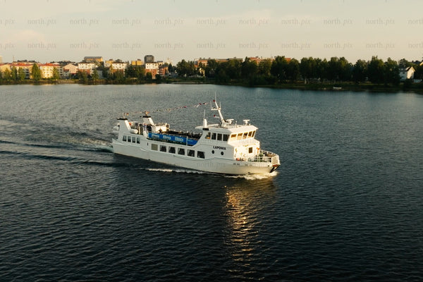 White passenger ferry gliding across calm lake near Luleå city center with trees and buildings