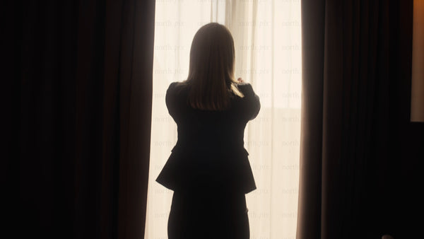 Businesswoman opens curtains in hotel room at sunrise in Luleå
