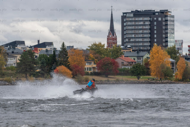 Person on jet ski near waterfront town in autumn