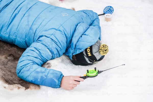 Person ice fishing on snow in winter wearing blue jacket