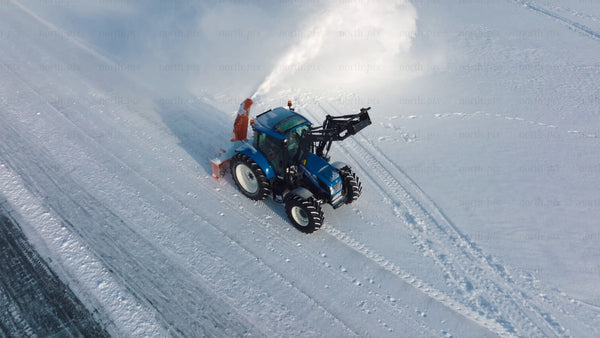 Snowplow tractor clearing icy road in winter, Luleå - aerial drone footage