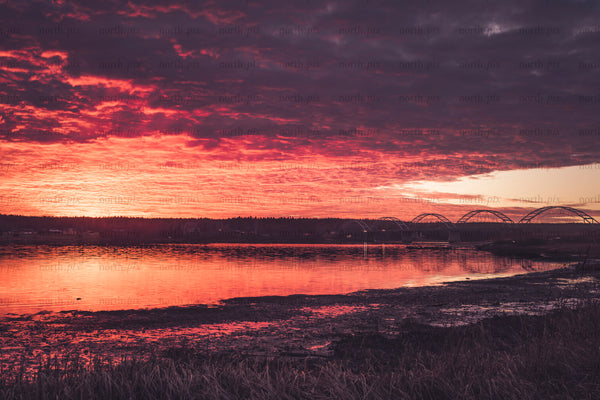 Arched bridge over river under red sunset sky