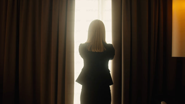 Businesswoman opens curtains in hotel room to bright sunny day