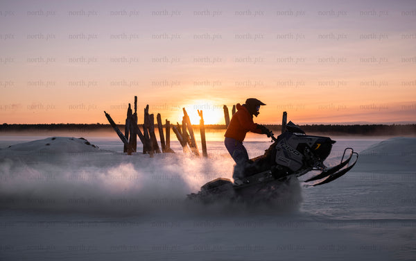 Snowmobile rider on a frozen lake at sunset