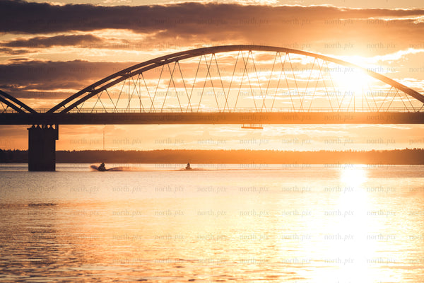 Arch bridge at sunset over calm water with jet skis