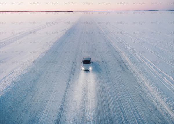 White car driving on a snowy ice road during sunset in winter