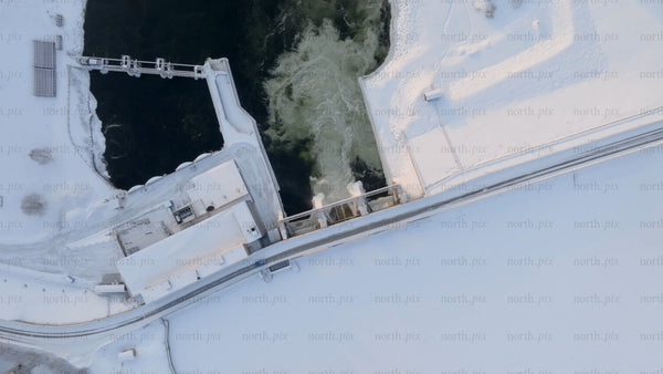 Aerial top down view of a hydroelectric power plant dam spilling water in snowy winter