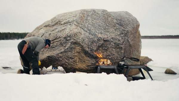 Winter Cooking in the Luleå Archipelago: Man Prepares a Meal by a Campfire on a Frozen Lake in Sweden