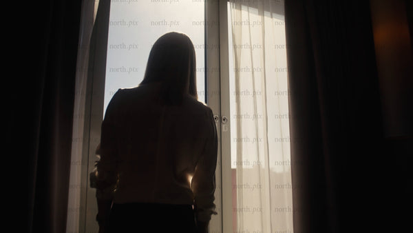 Woman in hotel room looks out window at sunrise in Luleå